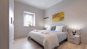 Ein Schlafzimmer mit Bett, Nachttischen, einem Fenster und einem Bild an der Wand.