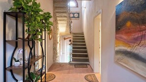 Ein Flur mit einer Treppe, einem schwarzen Metallregal mit Pflanzen und einem Gemälde an der Wand.