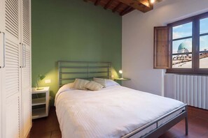 Ein Schlafzimmer mit Metallbettgestell, grüner Wand, Fenster mit Blick auf eine Kuppel und einem weißen Heizkörper.