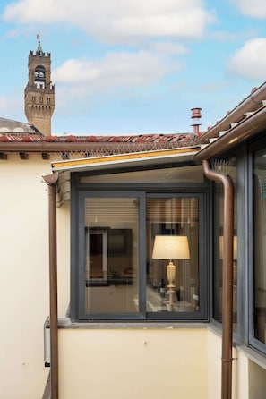 Eine Gebäudeecke mit einem Fenster, einer Lampe im Inneren und einem Turm im Hintergrund.