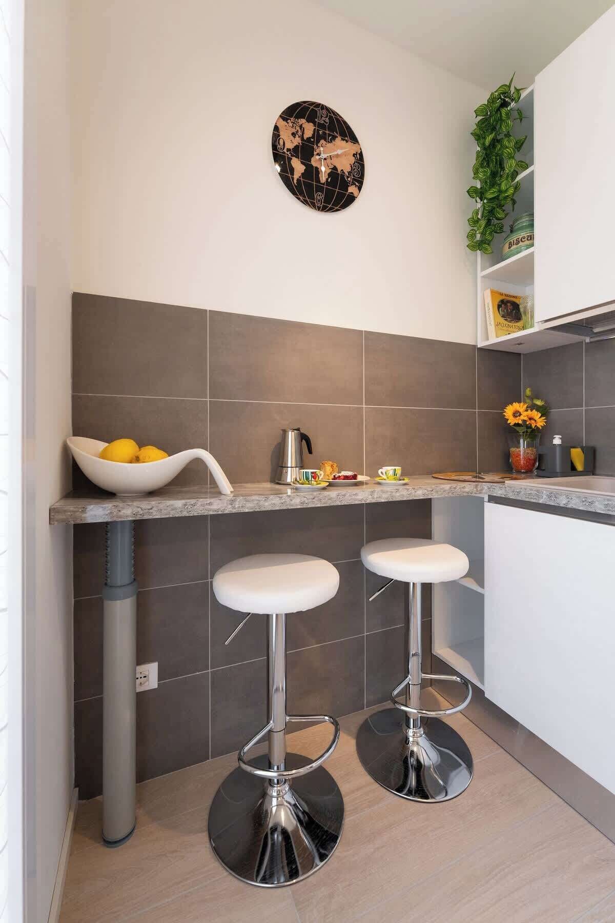 A modern kitchen with two bar stools, a world map clock, and a potted plant.