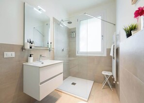 Une salle de bain moderne équipée d’une douche, d’un lavabo, d’un miroir et d’un petit tabouret.