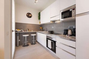 A modern kitchen with white cabinets, a stainless steel microwave, a gas stove, and a bar stool. - Giano - Conventino Modern - Apt con Garage (Firenze)