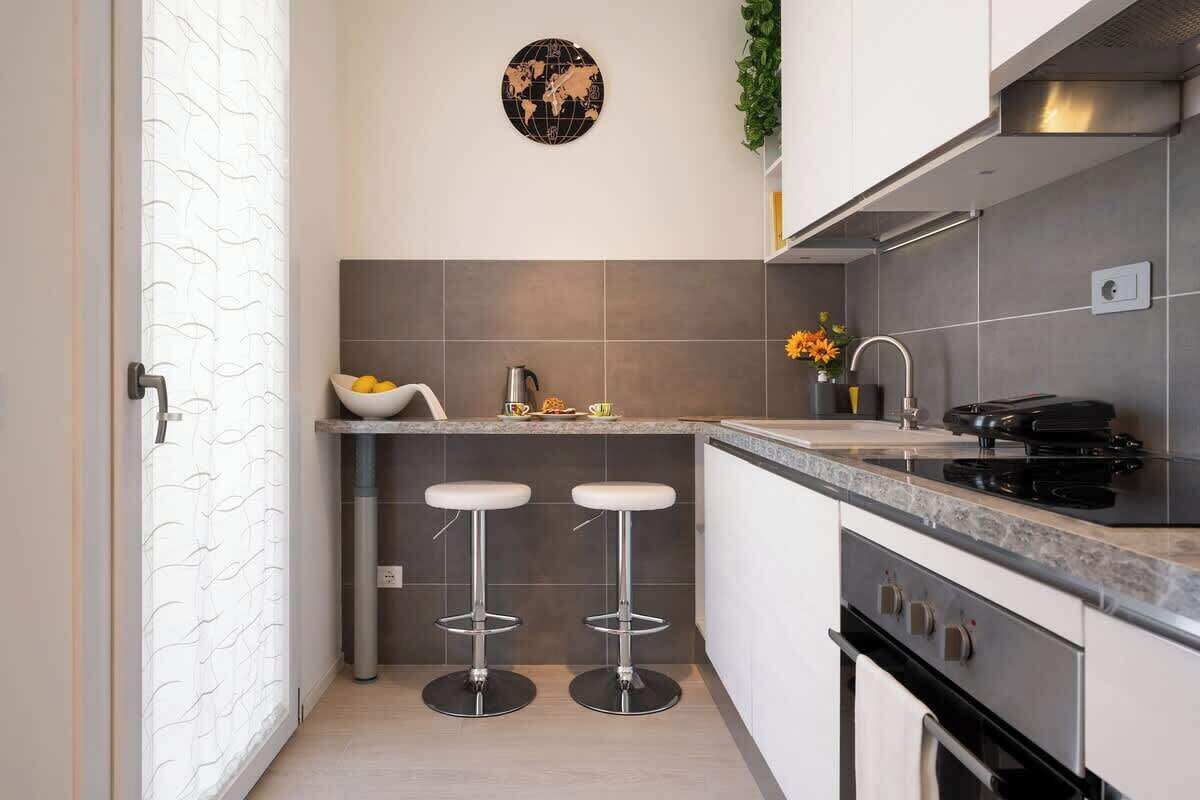 A compact kitchen with a stove, sink, two bar stools, and a small island with a bowl of lemons.
