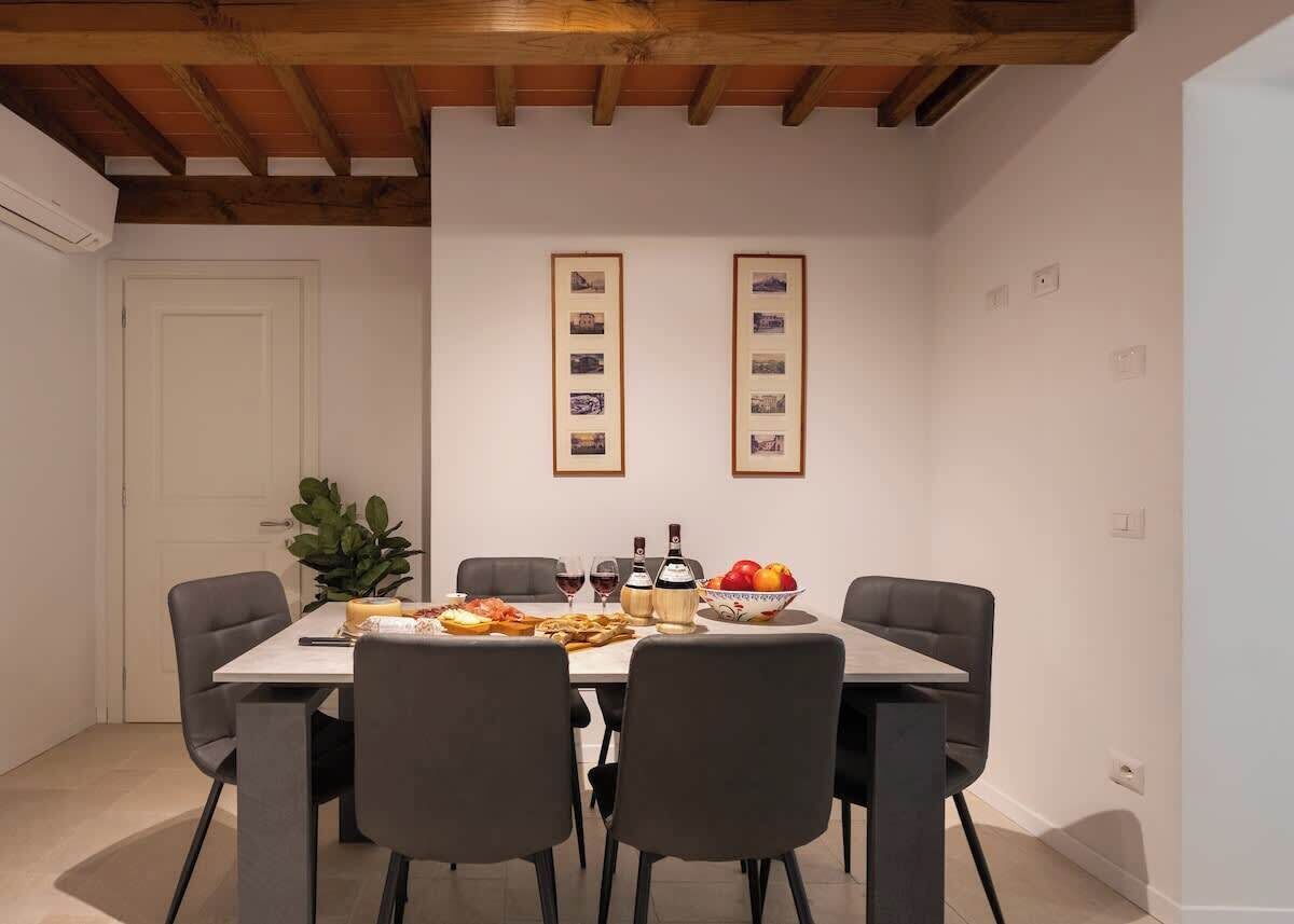 Uma área de refeições com uma mesa posta para quatro pessoas, duas fotos emolduradas na parede e um vaso de planta à esquerda.