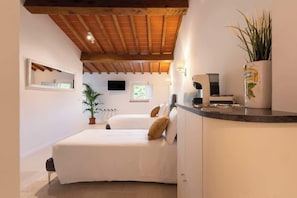 A bedroom with two beds, a wooden ceiling, a TV, a plant, and a kitchen counter. - Casa Falorni, 3 a+b - Pia e Simonetta - Trilocale (Greve in Chianti)