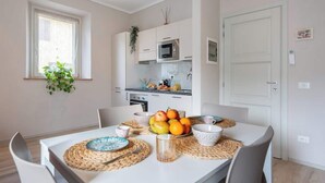 A modern kitchen with white cabinets, a microwave, and a sink. There is a dining table with placemats and fruit. - Civette 1, Studio Apt with Shared Garden View (Greve in Chianti)