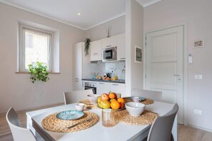 A modern kitchen with white cabinets, a microwave, and a sink. There is a dining table with placemats and fruit. - Civette 1, Studio Apt with Shared Garden View (Greve in Chianti)