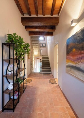 A hallway with a staircase, a black metal shelving unit with plants, and a painting on the wall. - Civette 1, Studio Apt with Shared Garden View (Greve in Chianti)