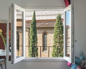 Ein offener Balkon mit Blick auf ein historisches Gebäude und zwei hohe Bäume.