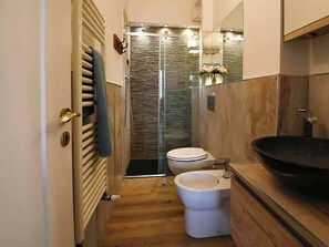 Un baño moderno con ducha, dos inodoros, un lavabo grande y un tocador de madera.