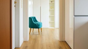 Ein Flur mit Holzboden, einem türkisblauen Sessel, einem weißen Schrank und einer Tür mit Messinggriffen.