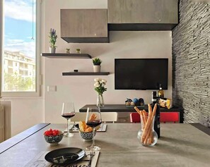 A modern dining area with a table set for two, a TV mounted on the wall, and a stone-textured wall. - Baracchini - Simona and Luca's Bright House (Firenze)