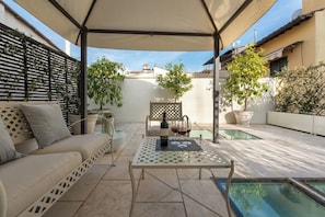 Eine möblierte Terrasse im Freien mit überdachtem Sitzbereich, einem Tisch mit Flasche und Gläsern sowie einem Pool.