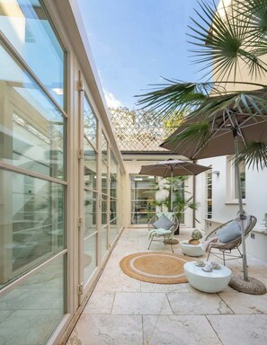 A modern patio with glass doors, outdoor seating, and a palm tree. - Luxury San Frediano Apartment: Parking & Gym Included (Firenze)