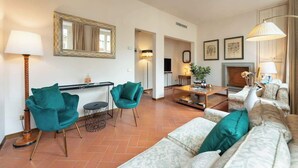 Una sala de estar con un sofá, dos sillones azul turquesa, una mesa de centro, una chimenea y un espejo en la pared.