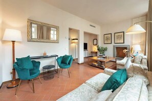 A living room with a sofa set, two teal chairs, a coffee table, a fireplace, and a mirror on the wall. - Antonella Elegant 3-Bedroom in Prime Location (Firenze)