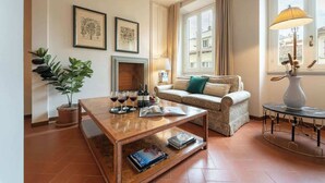 Una sala de estar con sofá, mesa de centro, chimenea, planta en maceta y ventana con cortinas.