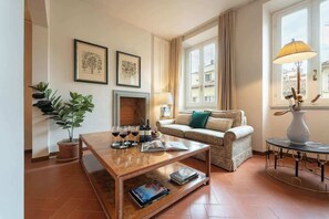 A living room with a sofa, coffee table, fireplace, potted plant, and a window with curtains. - Antonella Elegant 3-Bedroom in Prime Location (Firenze)