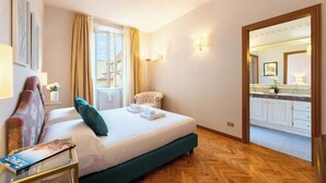 Una habitación de hotel con una cama, una silla, una mesa con una revista, una ventana con cortinas y vista a la cocina.