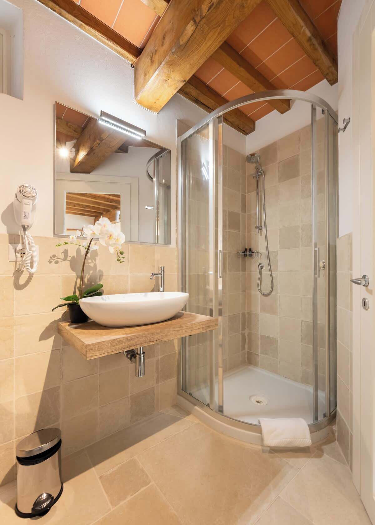 Ein modernes Badezimmer mit einer gläsernen Duschkabine, einem Holzkosmetikschrank, einem großen Spiegel und einer Orchidee im Topf.