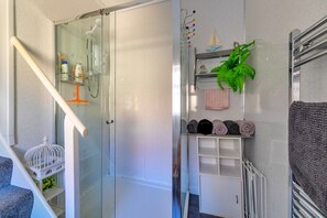 Ein Badezimmer mit Duschkabine aus Glas, einem weißen Handtuchhalter und einer Pflanze.