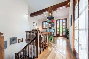 Eine Holztret Treppe mit Geländer, ein Bücherregal und eine Tür zu einem hellen Raum mit Tageslicht.
