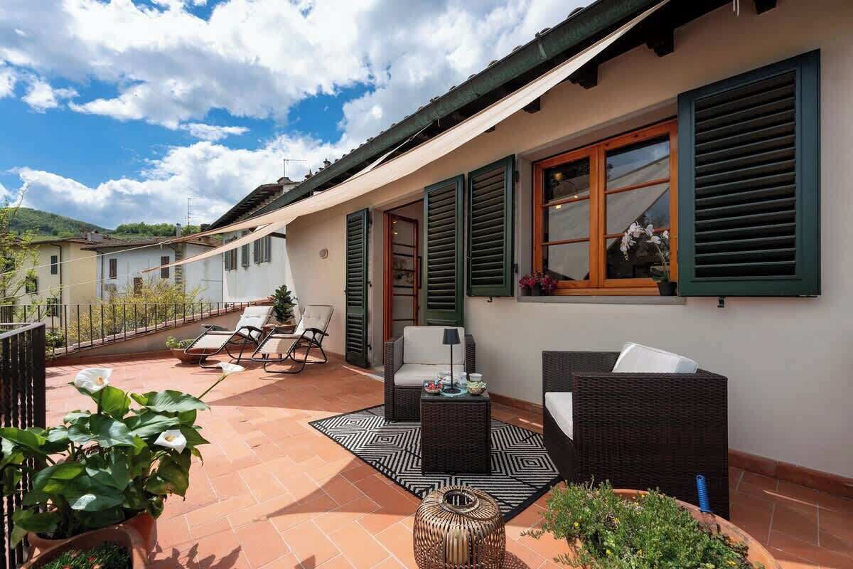 Eine Terrasse mit Gartenmöbeln, einem Rattansofa, einem Esstisch und Kübelpflanzen.