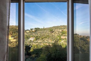 Vista dalla finestra su un paesaggio collinare con edifici sparsi e vegetazione.