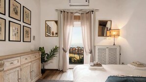 Quarto com cama, cômoda, espelho, luminária e vista para o exterior.