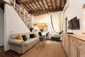 Un soggiorno con divano, tavolino, televisore e una scala con librerie.