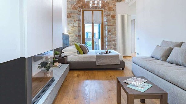 A modern bedroom with a stone archway, a bed, a sofa, and a TV. - Il toscano - Nuovo con terrazza in centro a Greve (Greve in Chianti)