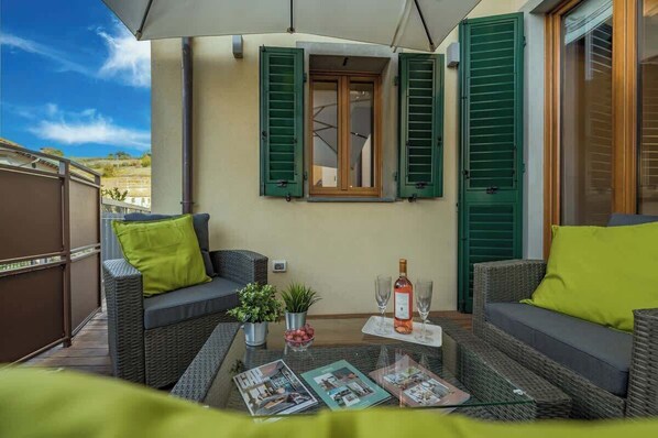Un balcone con mobili in vimini, un tavolo con riviste e una bottiglia di vino.