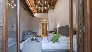 A bedroom with a bed, a sofa, a bedside table, a lamp, and a wooden ceiling. - Il toscano - Nuovo con terrazza in centro a Greve (Greve in Chianti)