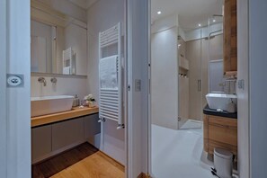 A modern bathroom with a large mirror, a white sink, a towel rack, a shower area, and a toilet. - Solatio · SoIatio - Incantevole con idromassaggio in centro (Greve in Chianti)
