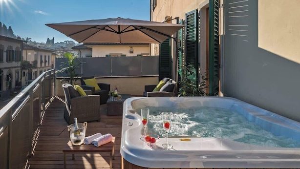 En takterrass med ett bubbelbad, utemöbler och ett stort parasoll.