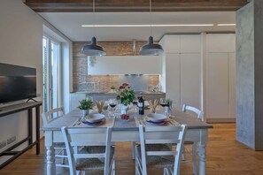 A modern dining area with a brick wall, pendant lights, and a kitchen in the background. - Solatio · SoIatio - Incantevole con idromassaggio in centro (Greve in Chianti)
