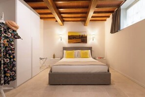 Ein Schlafzimmer mit Bett, Nachttisch, Wandlampe, einem Gemälde und einem Fenster mit Vorhängen.