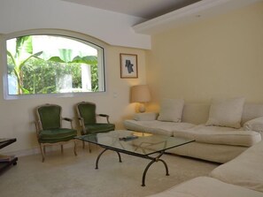 A living room with a glass coffee table, two green armchairs, a beige sofa, a lamp, and a window with a view of greenery. - Neo-Provencal villa with sea view (Vallauris)