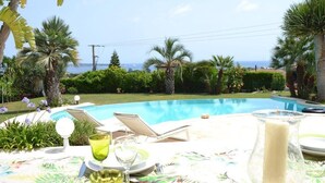 Une table placée au bord de la piscine, avec une bougie dans un photophore en verre, un verre d’eau et une chaise.