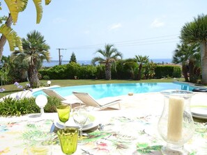 A poolside table with a glass candle, a glass of water, and a chair. - Neo-Provencal villa with sea view (Vallauris)