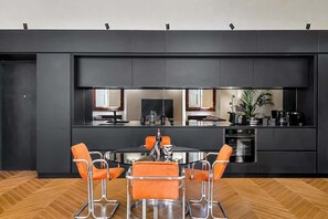 Eine moderne Küche mit Kochinsel, schwarzen Schränken und orangefarbenen Stühlen um einem runden Tisch.