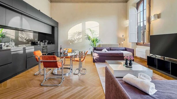 Ein modernes Wohnzimmer mit einer Couch, einem Couchtisch und einem Fernseher. Es gibt eine Küchenzeile mit einem Esstisch und Stühlen.