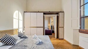 Ein Hotelzimmer mit Bett, Holz-Kopfteil, großem Fenster und Blick in das angrenzende Zimmer.