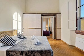Ein Hotelzimmer mit Bett, Holz-Kopfteil, großem Fenster und Blick in das angrenzende Zimmer.