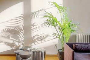 Ein Zimmer mit einer großen Kübelpflanze, einer Couch und Metallhockern.
