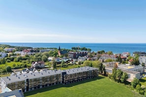 Ein Wohngebiet mit einem großen Gebäude, das mehrere Balkone aufweist, umgeben von Grünflächen und Blick auf das Meer.