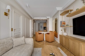 Ein modernes Wohnzimmer mit einer Couch, einem runden Tisch mit Stühlen, einem Fernseher und einer Holzkommode.