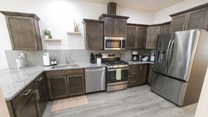 A modern kitchen with dark wood cabinets, stainless steel appliances, and a granite countertop. - This 3BR/2BA retreat. North End Haven | Steps from Parks, Trails & Local Favorites Walking distance to Hyde Park  and Camel’s back park | Close to Boise White Water park and E Bikes For Rent it simple at this peaceful and centrally-located place. (Boise)