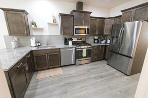 A modern kitchen with dark wood cabinets, stainless steel appliances, and a granite countertop. - This 3BR/2BA retreat. North End Haven | Steps from Parks, Trails & Local Favorites Walking distance to Hyde Park  and Camel’s back park | Close to Boise White Water park and E Bikes For Rent it simple at this peaceful and centrally-located place. (Boise)